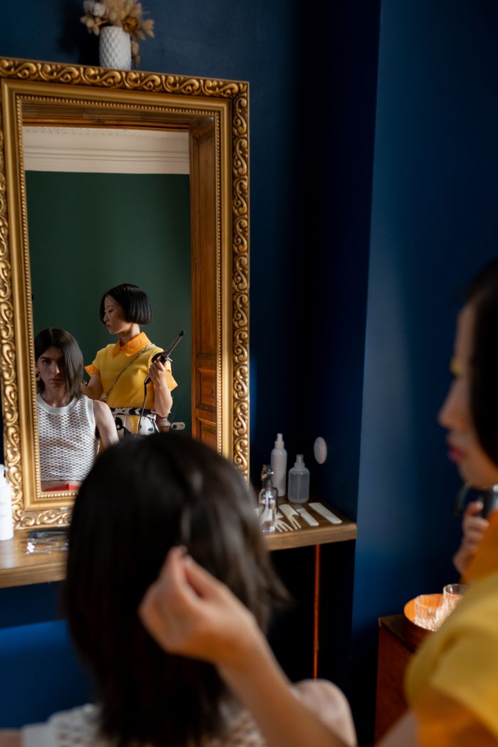 A hair stylist curling a client's hair in a modern salon, reflected in a mirror.