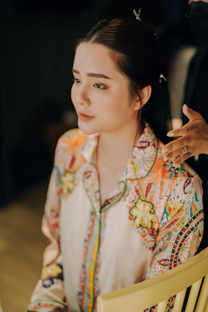A woman with long hair sitting indoors, wearing a colorful blouse, getting her hair styled.