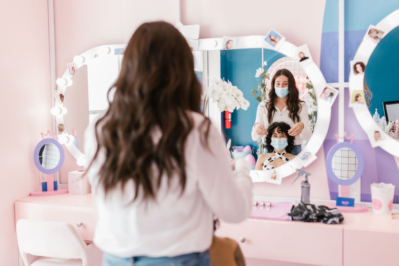 Hairdresser and client wearing masks in a modern salon, reflecting pandemic safety measures.